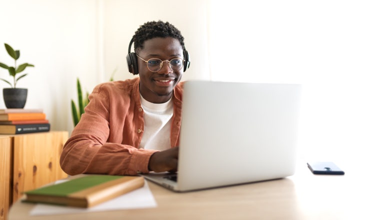 A man sitting at a table explores what a dissertation vs. thesis is on his laptop.