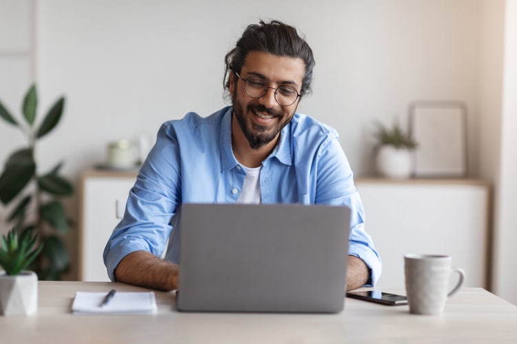 A man sitting at a table types on his laptop to create a tax invoice.