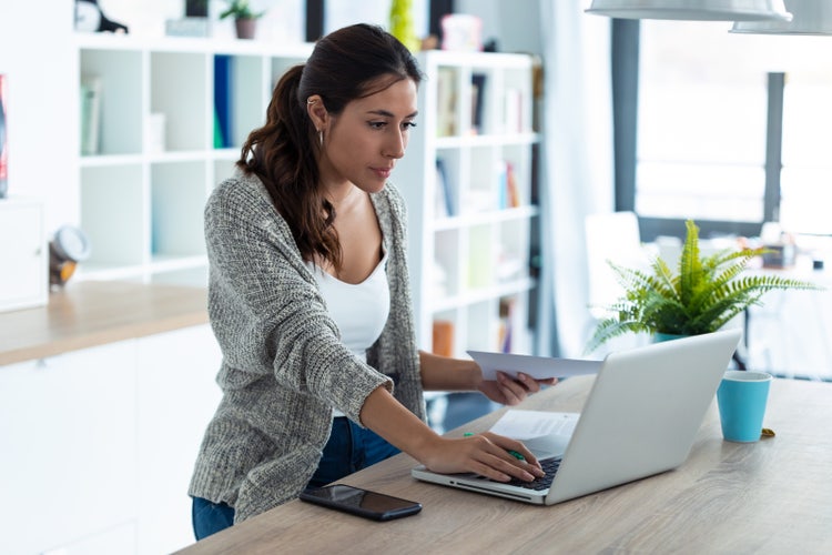 A woman standing at a desk creates an hourly invoice template on her laptop.