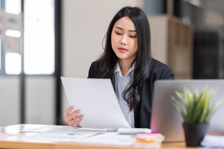 A woman sitting at a desk holds a piece of paper