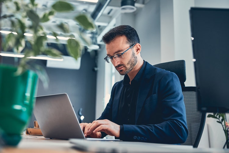 A man in an office uses his laptop to create a purchase order form template.