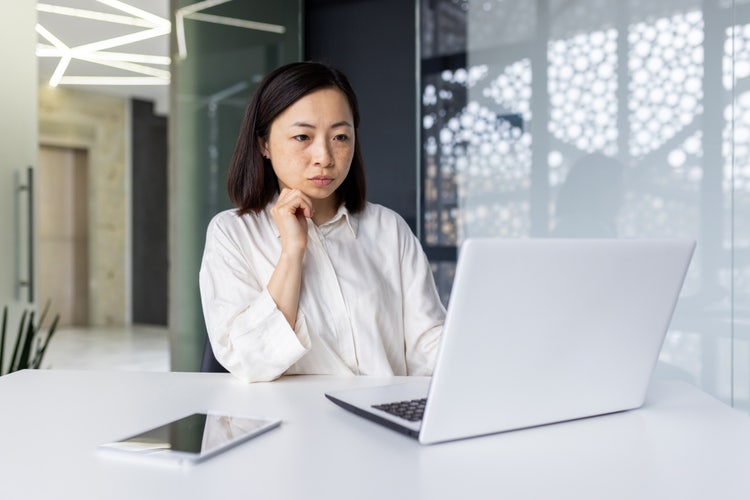 A woman sitting at a desk looks at her laptop
