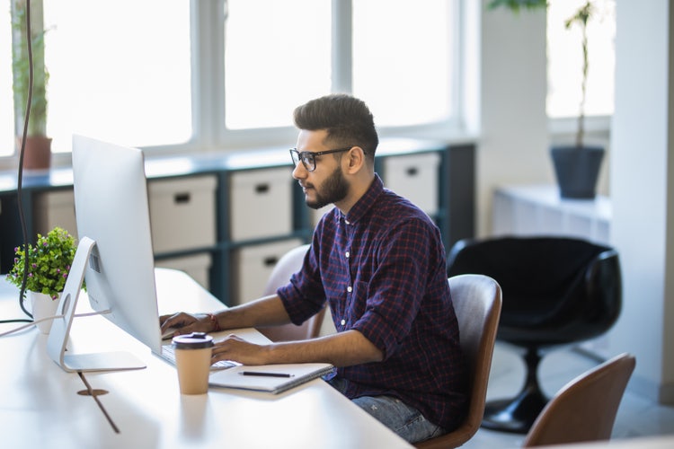 `A man sitting at a desk uses his computer to look through his company's paperless document management software