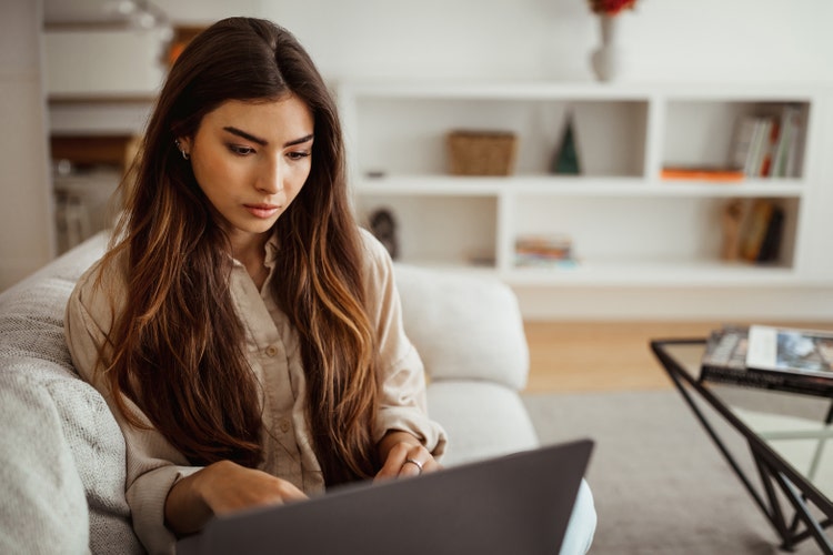 A woman sitting on a couch uses her laptop to learn what a clause in a contract is.