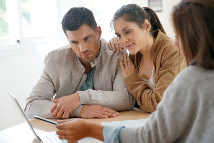 A couple and a real estate agent review a real estate purchase agreement together.