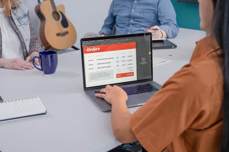 A woman sitting at a table with two people across from her creates a paperless billing document on her laptop.