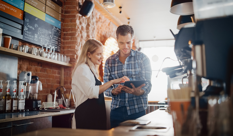 A barista and her employer look at a tablet to check time-tracking.