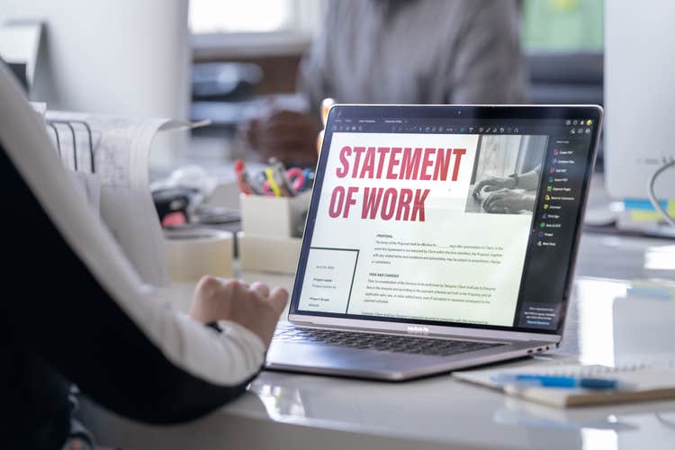 An office worker writes a bid proposal using a laptop.