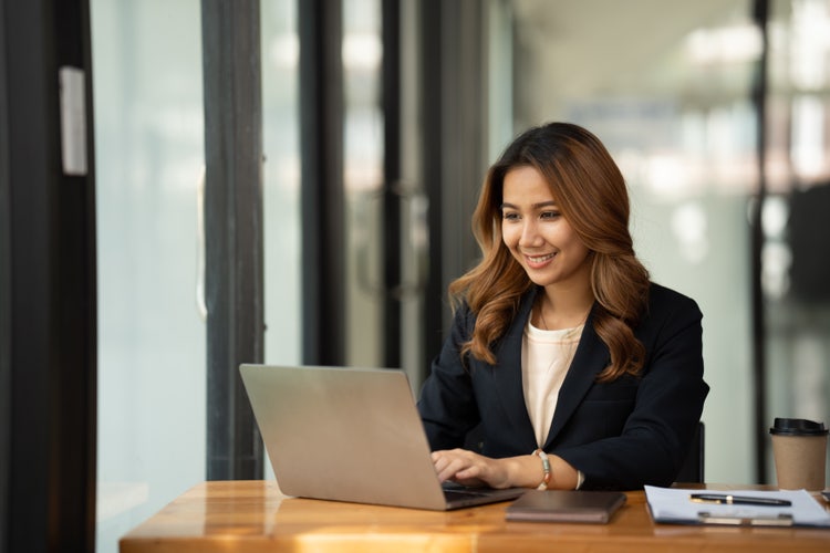 A woman sitting at a desk uses business process automation software on her laptop.
