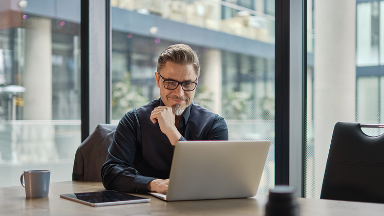 A man sitting at a desk looks at his laptop.
