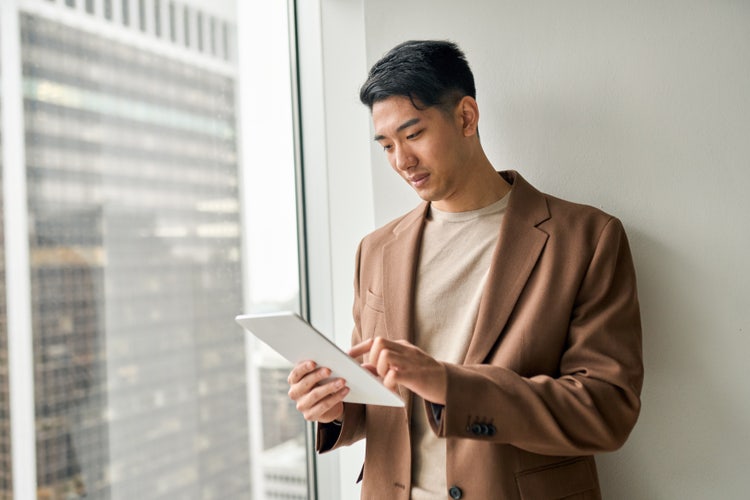 A man next to a window uses an e-signature software on his tablet to sign a digital document