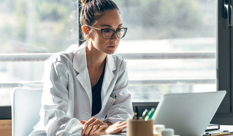 A woman in a lab coat looks at a laptop.