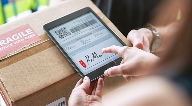 A close up of a woman's hands signing a bill of lading form for a package on a tablet.