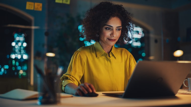 A person making a letter of interest on their laptop while sitting in the dark at a kitchen bar table