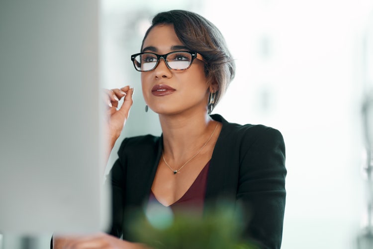 A businesswoman wearing glasses looks at a computer screen and reads about project planning tools.