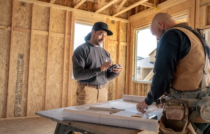 A photo of two contractors inside a room at a construction site. One of them is signing a contract electronically on a smartphone.