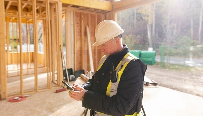 A subcontractor wearing safety equipment looking over an agreement on their phone