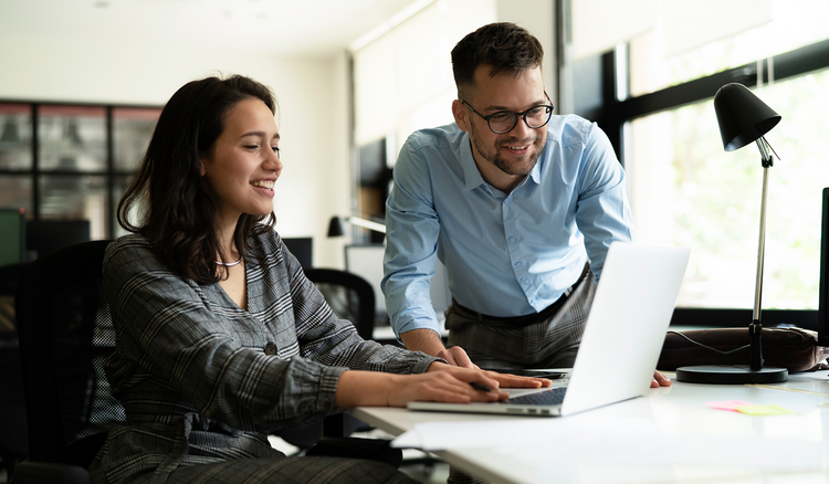 A man and a woman look at a laptop in an office space.