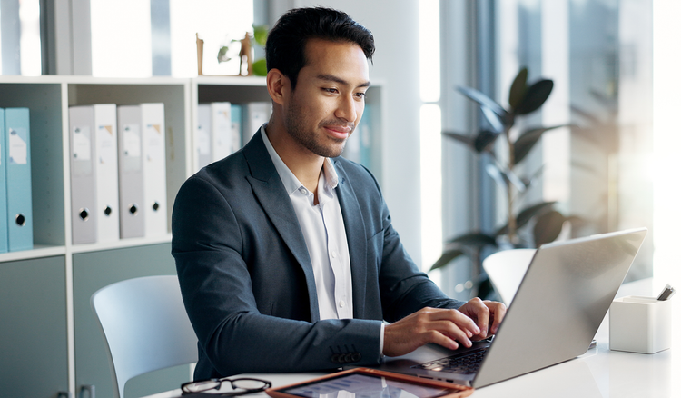 A man sitting at a desk types on his laptop.