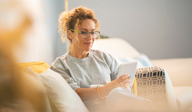A woman sitting on a couch holds a tablet device.