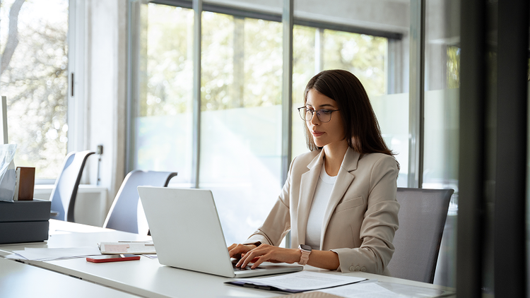 A woman sitting at a desk types on a laptop.