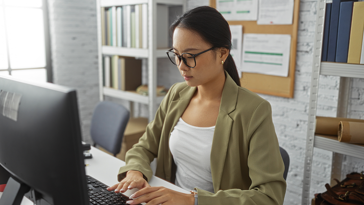 A woman sitting at a desk types on a desktop computer.