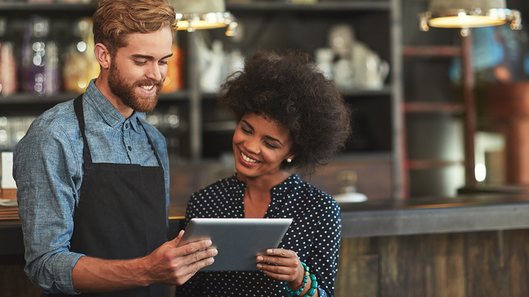 A man and a woman in a retail store hold a tablet.