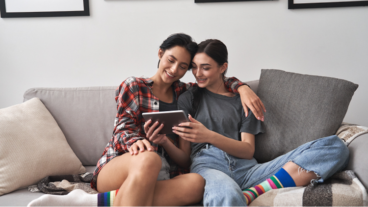 A couple searches rental properties on a tablet as they sit snuggling on the couch.