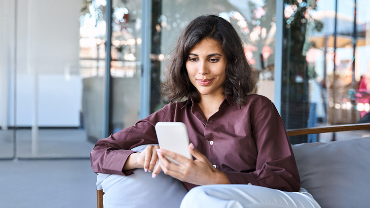 A woman sitting on a couch looks at her smartphone.