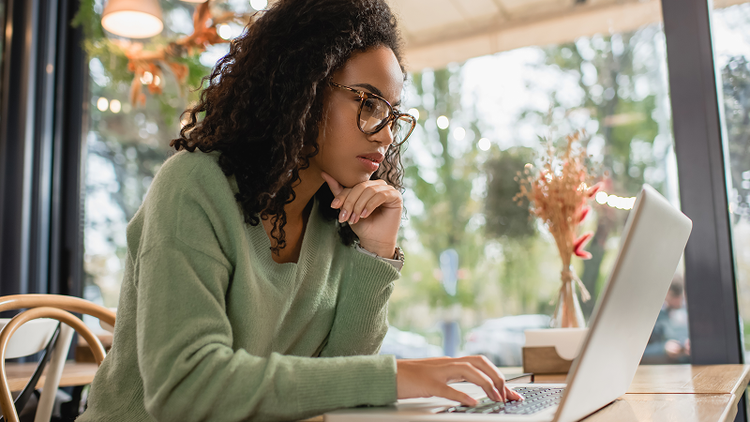 A woman sitting at a table looks at her laptop.