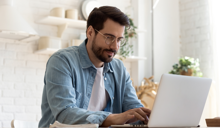 A man sitting at a table types on his laptop.