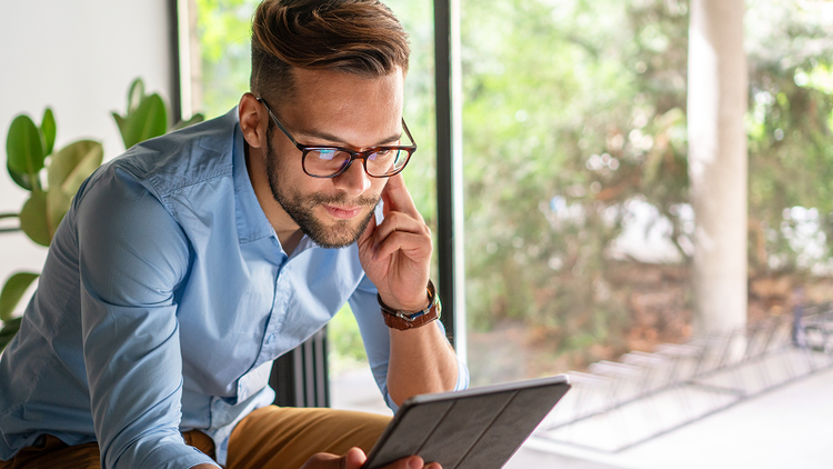 A man sits and looks at a tablet device.
