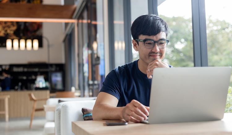 A man sitting at a table looks at his laptop.