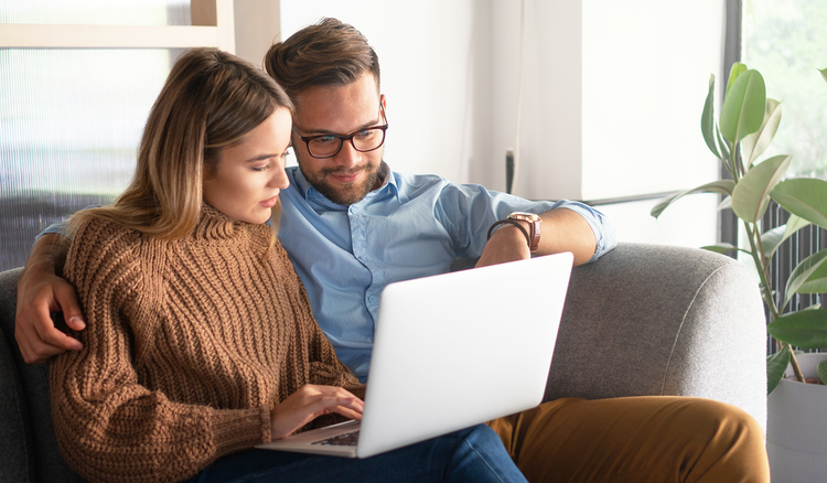 A man and a woman sit on a couch and look at a laptop.