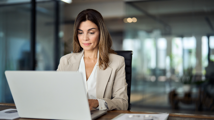 A woman sitting at a desk types on a laptop.