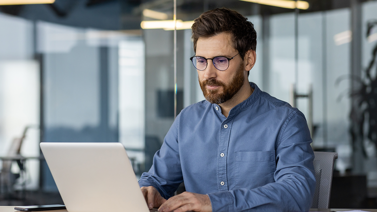A man sitting at a desk types on his laptop.