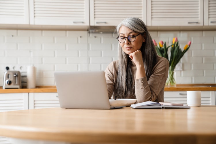 A landlord sitting at a desk reviewing a printed apartment lease agreement while using their laptop.