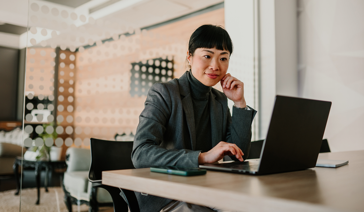 A woman sitting at a table types on her laptop.