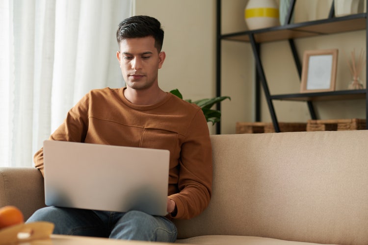 A young man working on a laptop in a home living room environment.