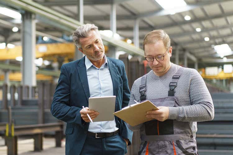 Two people standing in a factory and filling out some forms.