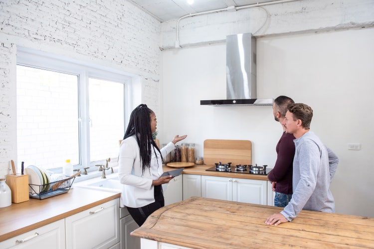 A landlord and two potential tenants looking at a kitchen of an apartment.