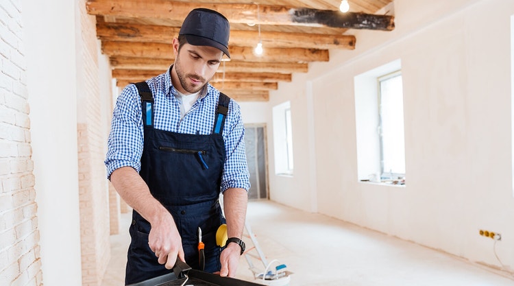 A paint contractor dipping a paint roller into a roller tray at a job site