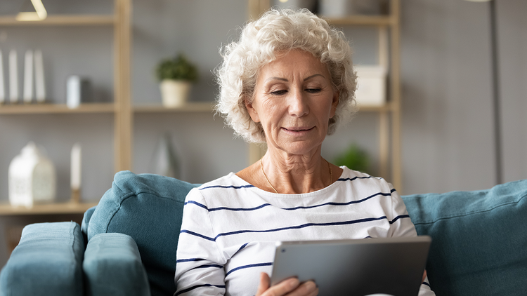 A woman sitting on a couch looks at her tablet device.