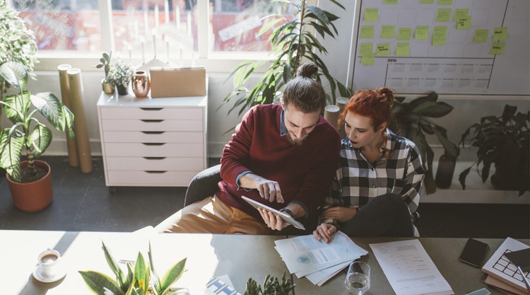 Two people sitting at a large table reviewing grant proposals and looking at a tablet device together