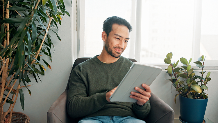 A man sitting in a chair uses a tablet device.