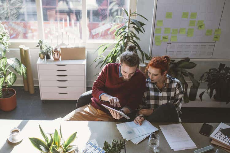 Two people sitting at a large table reviewing grant proposals and looking at a tablet device together