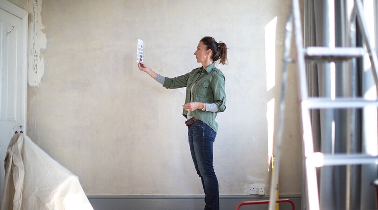 A female contractor determining a paint color for a wall by holding up a paint color palette