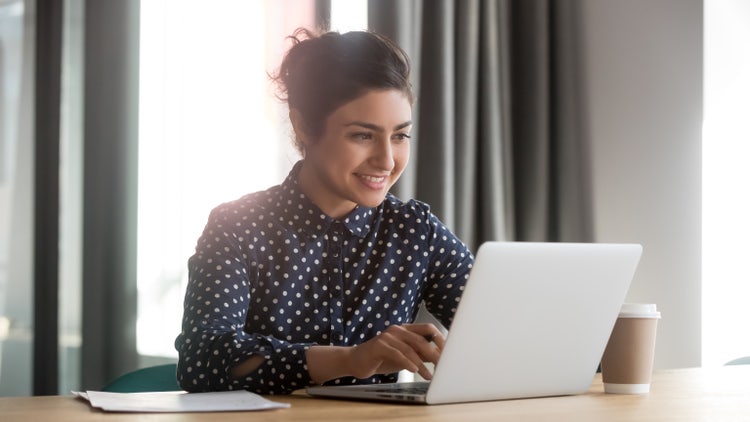 A woman sitting at a table builds a new client intake form on her laptop.