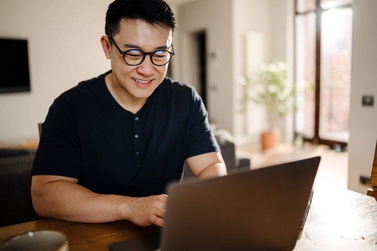 A man working from home uses a Mac laptop to type in a PDF file.