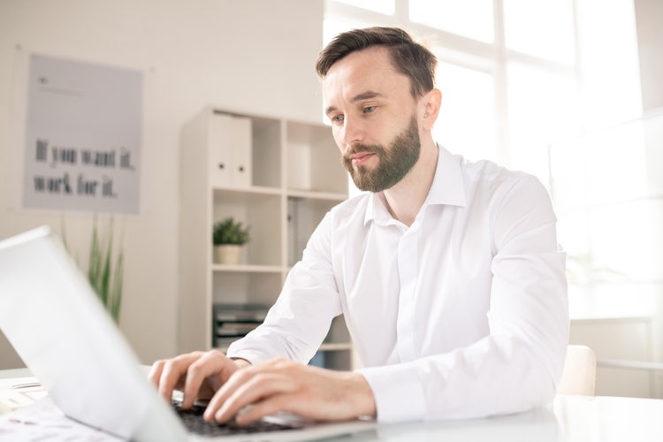 A man at a desk using a laptop computer to save a PowerPoint presentation as a PDF with notes.